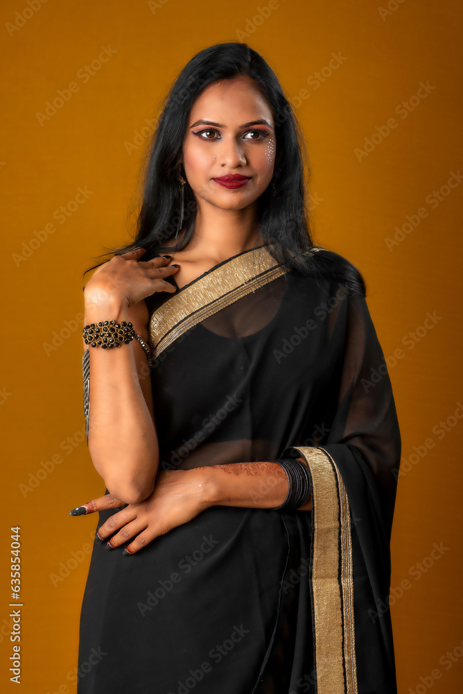 Portrait of a young beautiful girl wearing traditional black saree posing on a brown background. Portrait of a young beautiful girl wearing traditional black saree posing on a brown background.