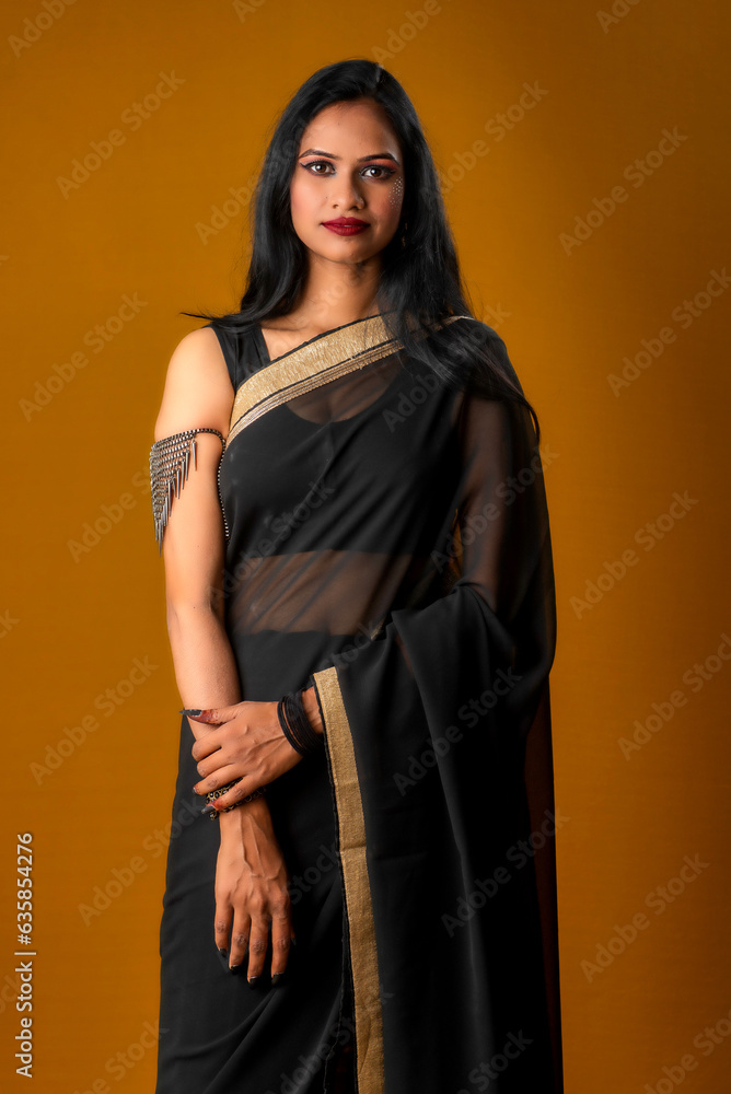 Portrait of a young beautiful girl wearing traditional black saree posing on a brown background. Portrait of a young beautiful girl wearing traditional black saree posing on a brown background.