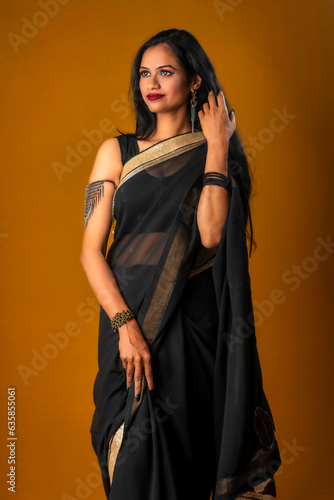 Portrait of a young beautiful girl wearing traditional black saree posing on a brown background. © Dip Photography