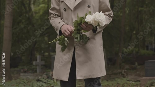 Unrecognizable widower bringing bouquet of white roses to grave of his beloved wife