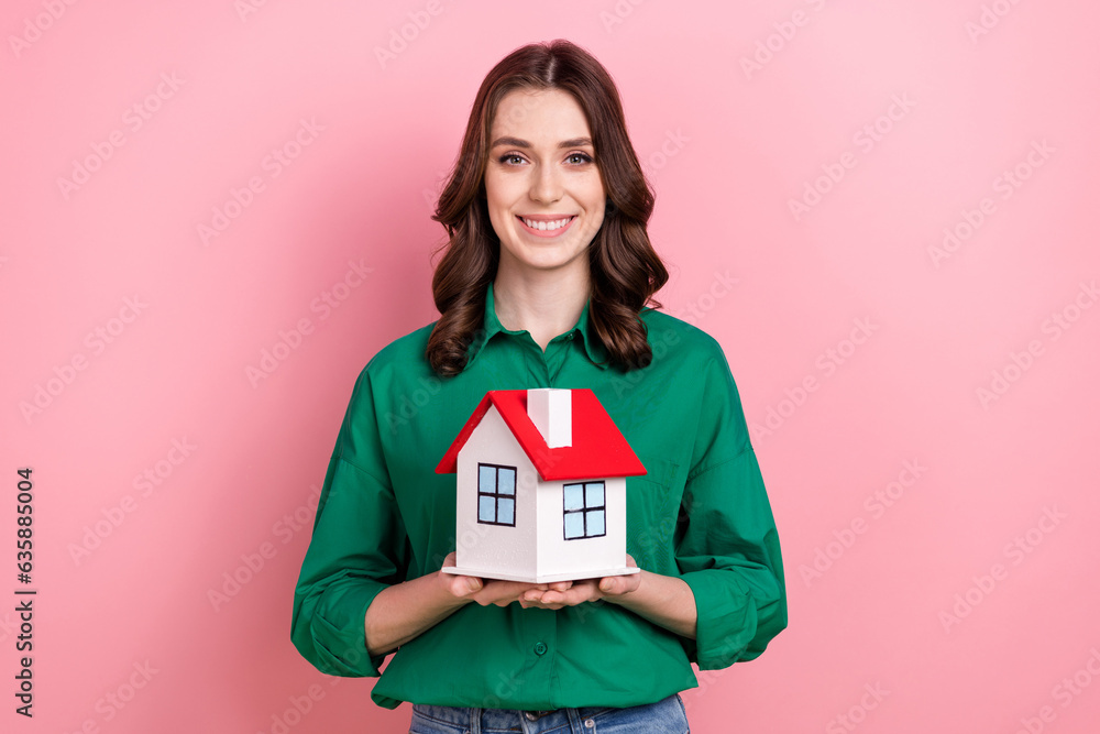 Photo of cute cheerful woman dressed green shirt holding arms small house isolated pink color background Photo of cute cheerful woman dressed green shirt holding arms small house isolated pink color background