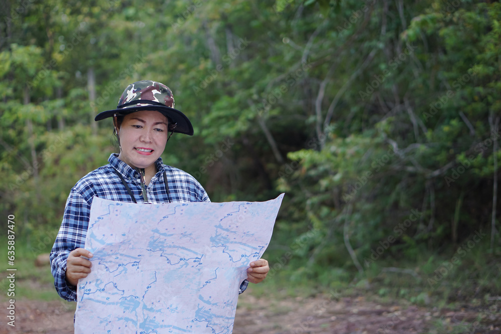 Asian woman explorer holds paper map to survey route in forest. Concept, travelling, nature exploration. Ecology study. Pastime activity, Adventure lifestyle. Explore environment.     