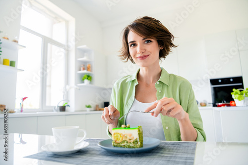 Photo of cheerful positive girl wear green shirt enjoying fresh backed cake piece indoors kitchen room