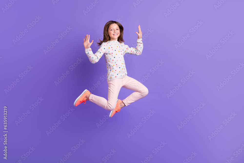 Full length photo of excited funky small girl wear dotted sweater jumping high isolated violet color background