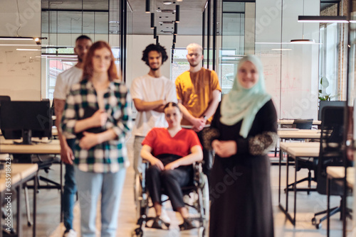 A diverse group of young business people congregates within a modern startup s glass-enclosed office  featuring inclusivity with a person in a wheelchair  an African American young man   and a hijab