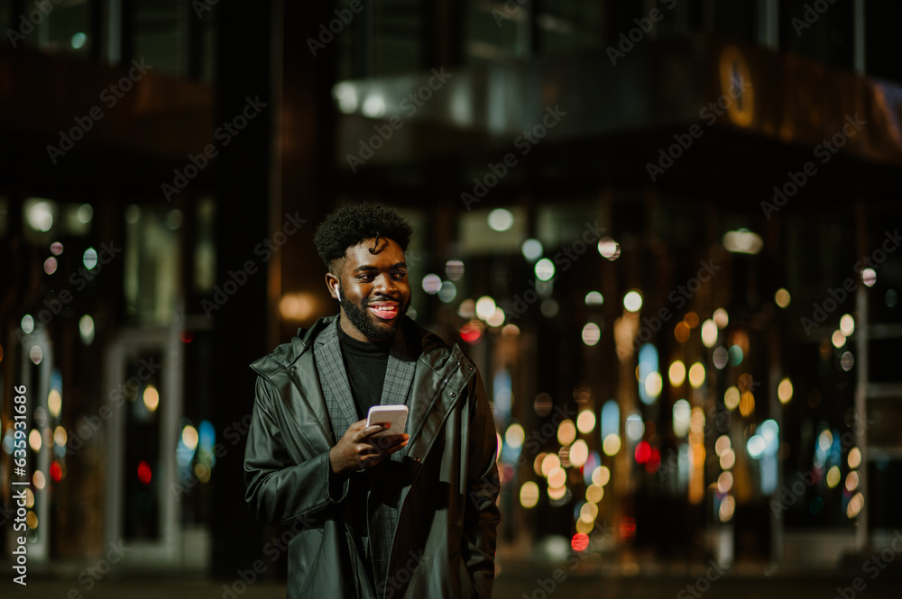 A happy African American man having a night-time call on the city street during his walk.