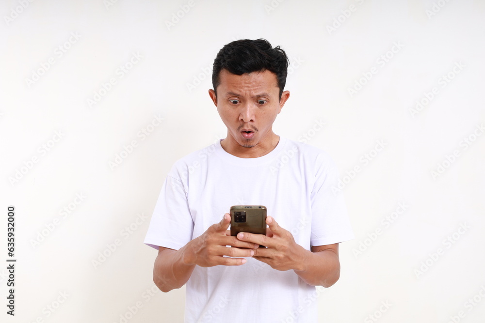 Shocked asian funny man standing while holding a cell phone. Isolated on white background Shocked asian funny man standing while holding a cell phone. Isolated on white background