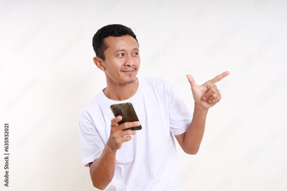 Happy asian funny man holding a cell phone while pointing sideways. Isolated on white background Happy asian funny man holding a cell phone while pointing sideways. Isolated on white background
