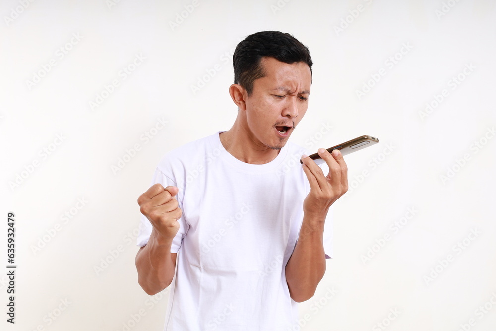 Angry asian funny man standing while on phone with loud speaker mode. Isolated on white background Angry asian funny man standing while on phone with loud speaker mode. Isolated on white background