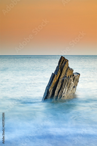 A sunset view of a jagged tooth-like rock, surrounded by surging sea at Ayrmer Cove, a remote cove near Kingsbridge, south coast of Devon, England, United Kingdom photo