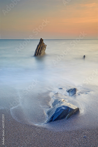 Surf rolls around shoreline rocks at sunset, in Ayrmer Cove, a remote cove near Kingsbridge, south coast of Devon, England, United Kingdom photo