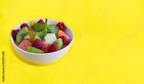 Fruit  salad in the white  bowl on the yellow background. Copy space.