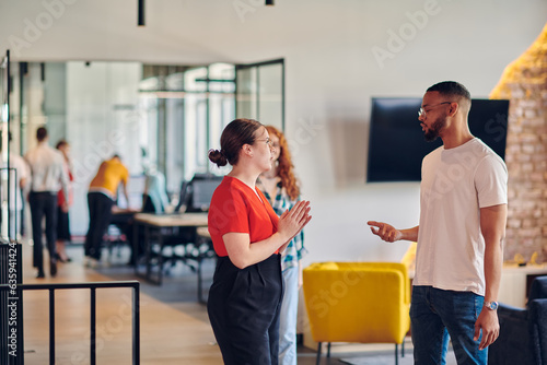 Young group of business colleagues, including an African American businessman, engage in a conversation about business issues in the hallway of a modern startup coworking center, exemplifying dynamic