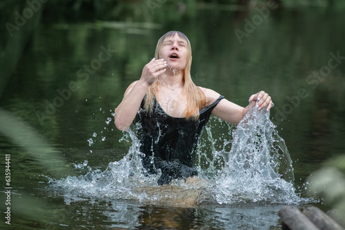 A young beautiful blonde girl jumps out of the water.