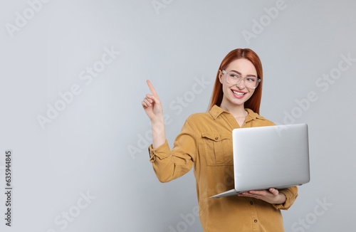 Smiling young woman with laptop on grey background, space for text