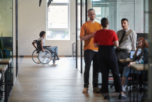 A diverse group of colleagues engages in a discussion about business challenges within a modern coworking startup center, while in the background, their wheelchair-bound colleague symbolizes