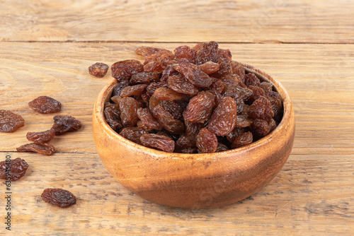 Sweet dehydrated raisins in a bowl and on a wooden background.