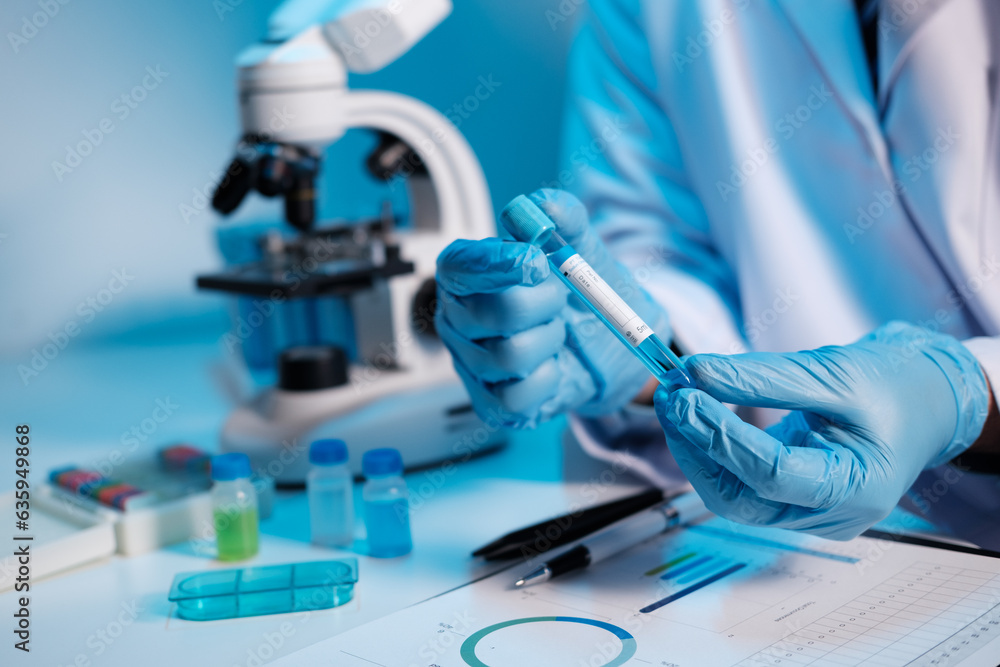 Fototapeta premium Scientist hand taking a sample tube from a rack with machines of analysis in the lab background, Technician holding tube test in the research laboratory.