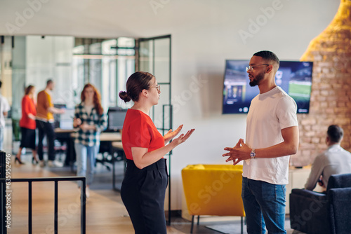 Young business colleagues, including an African American businessman, engage in a conversation about business issues in the hallway of a modern startup coworking center, exemplifying dynamic problem