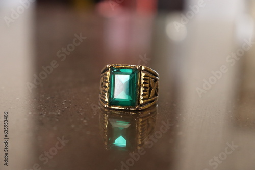 An Ancient Golden Ring embedded with Green Emerald Stone Gem on a shiny brown marble 