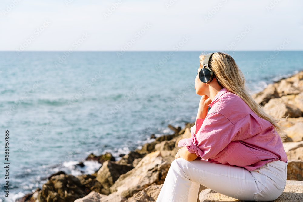 Woman sitting near waving seashore and listening to music