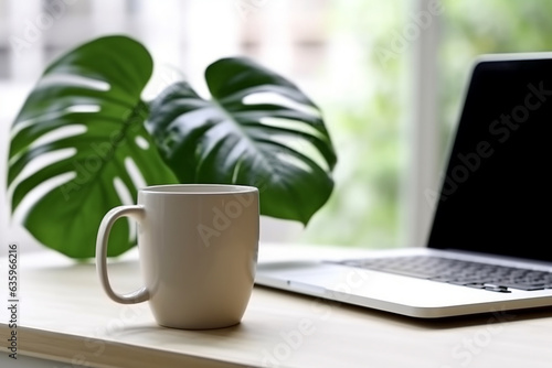 Coffee cup and monstera plant leaf with laptop on table.