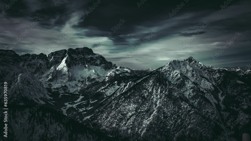 Aerial view of the majestic Jof di Montasio mountain in Italy, surrounded by a dramatic cloudy sky. Aerial view of the majestic Jof di Montasio mountain in Italy, surrounded by a dramatic cloudy sky.