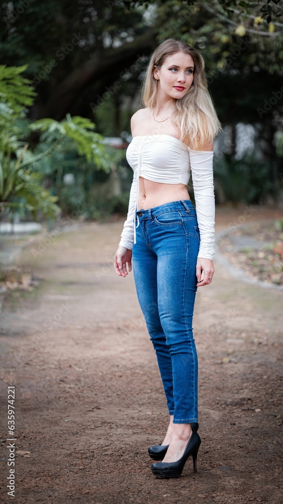 Obraz premium Blonde girl in a white top and blue jeans posing outdoors