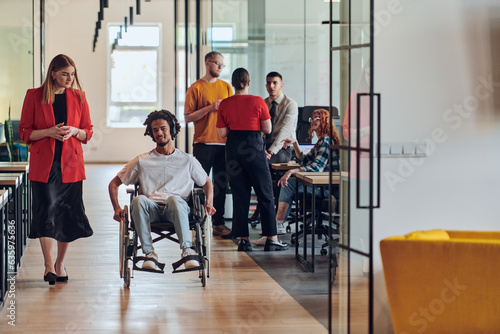 A group of young business people in a modern glass-walled office captures the essence of diversity and collaboration, while two colleagues, including an African American businessman in a wheelchair © .shock
