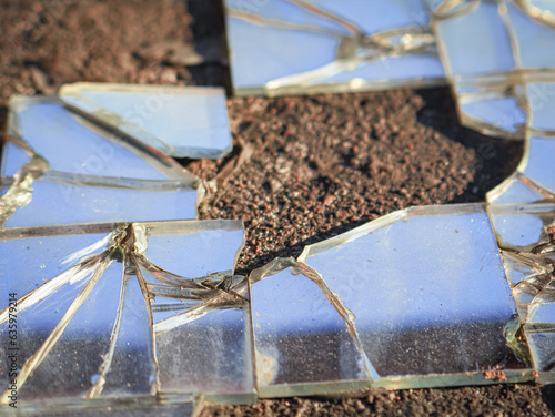 Shards of broken mirror glass on the concrete floor in warm sunlight with reflection of the blue sky