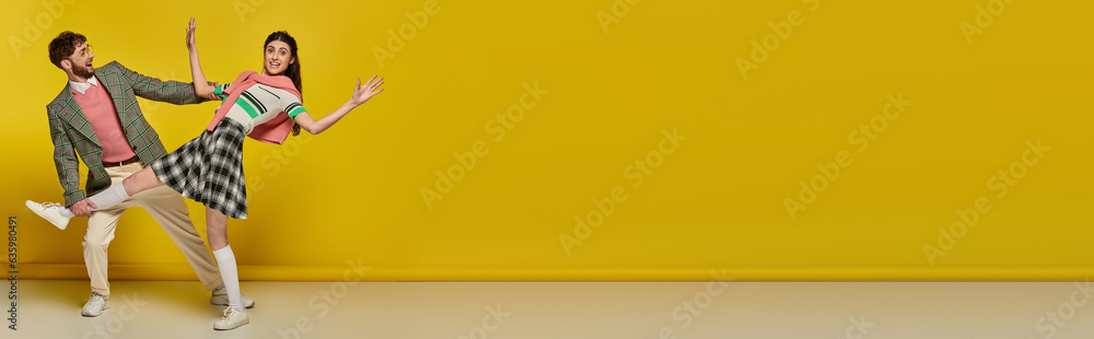 Obraz premium cheerful man in glasses catching falling woman, young couple, funny, yellow backdrop, banner