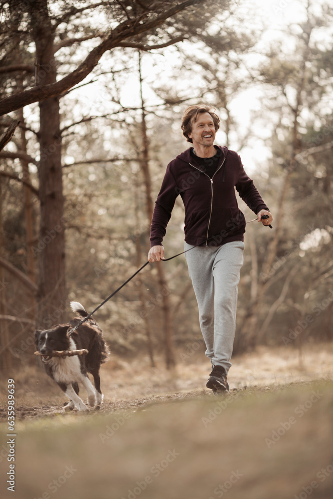 Middle aged caucasian man jogging and exercising with his border collie dog in a forest park Middle aged caucasian man jogging and exercising with his border collie dog in a forest park