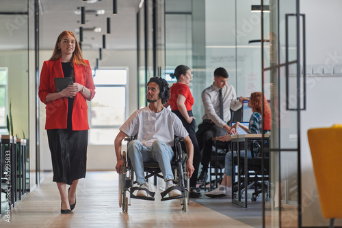 A group of young business people in a modern glass-walled office captures the essence of diversity and collaboration, while two colleagues, including an African American businessman in a wheelchair