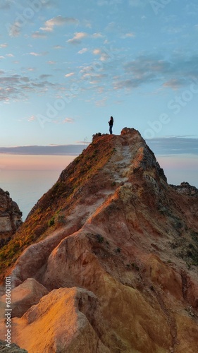 Vertical of a woman standing on a rocky mountaintop at sunset at Portugese coastline