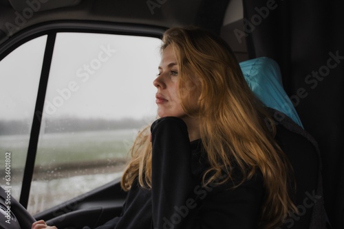woman sitting in front of steering wheel inside car while rain falls down © Trio Stories/Wirestock Creators