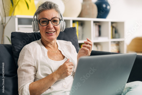 Senior woman with headset is using laptop at home.