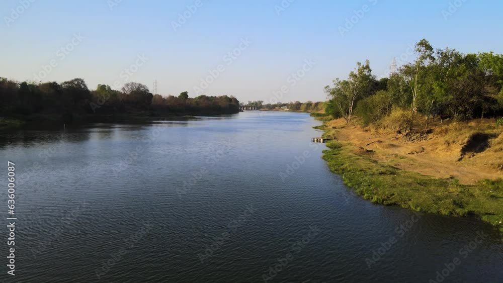 Aerial shot of a river flowing through its banks covered with greenery on a sunny day Aerial shot of a river flowing through its banks covered with greenery on a sunny day