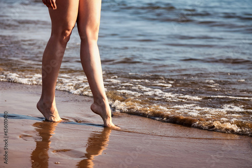 Crop photo of naked legs woman nudist walking on sea beach outdoors, close up. Foots of nude young sexy lady step on water, natural idyllic lifestyle. Nudism naturism concept. Copy ad text space