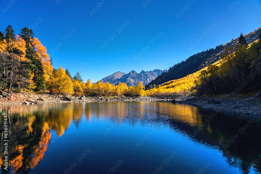 Obraz premium Beautiful landscape with mountain lake and high rocks with illuminated peaks reflection with green water, blue clean sky and yellow autumn sunrise.