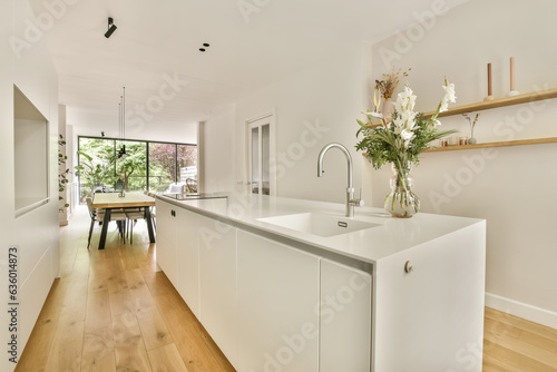 a kitchen and dining area in a house with wood flooring  white cabinets and an open door leading to the patio