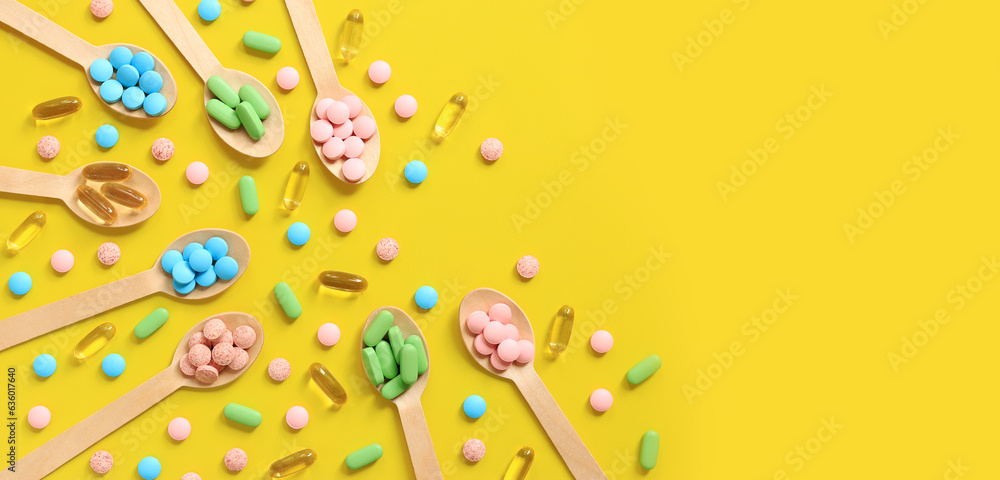 Vitamins of different colors in wooden spoons on a yellow background. Top view of scattered bright pills. Pharmaceutical industry. Health care and medicine. Pharmacy product. Copy space Vitamins of different colors in wooden spoons on a yellow background. Top view of scattered bright pills. Pharmaceutical industry. Health care and medicine. Pharmacy product. Copy space
