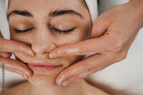 Foto Close-up view of a beautiful woman lying with closed eyes at spa while a massage therapist is massaging her face