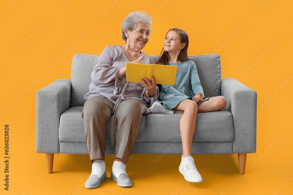 Little girl with her grandmother reading book on yellow background Little girl with her grandmother reading book on yellow background