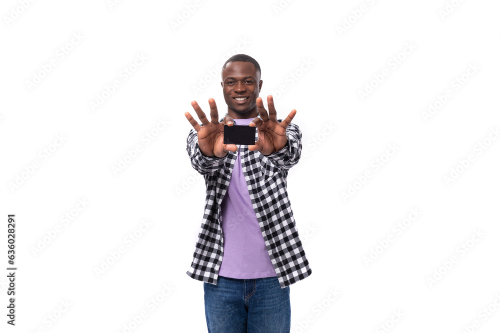 handsome 30 year old african manager guy dressed in a plaid shirt shows a mockup of a credit card on the background with copy space handsome 30 year old african manager guy dressed in a plaid shirt shows a mockup of a credit card on the background with copy space