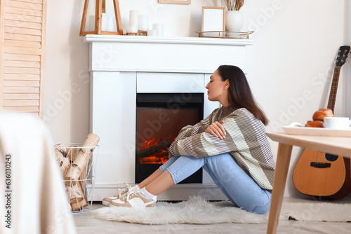 Frozen young woman warming near fireplace at home