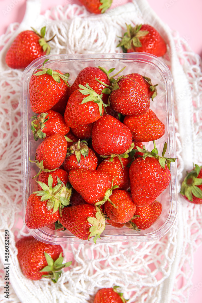 Mesh bag with fresh strawberry in plastic container on pink background, closeup Mesh bag with fresh strawberry in plastic container on pink background, closeup