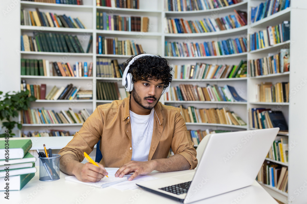 Serious concentrated man in headphones studying in library, hispanic student thinking and recording video course while sitting in university campus library. Serious concentrated man in headphones studying in library, hispanic student thinking and recording video course while sitting in university campus library.