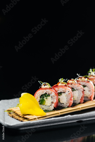 Tuna Dragon sushi with tuna, tiger shrimp, cream cheese, cucumber, tobiko caviar, Spicy sauce, Unagi sauce on a board made of wooden sticks tied with thread