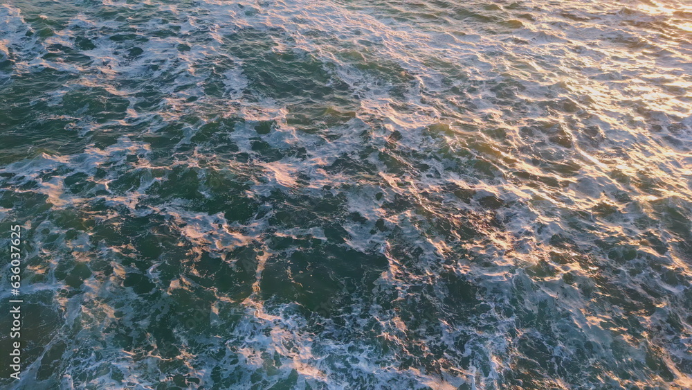 Drone view rough ocean water surface at golden sunset light. High coastal rock