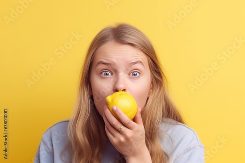 Blond European Child Eating Lemon, Creating a Grimace and Squeezing Eyes Amidst a Yellow Background, Displaying Humorous Expressions in Response to the Sour Taste of Fresh Fruits